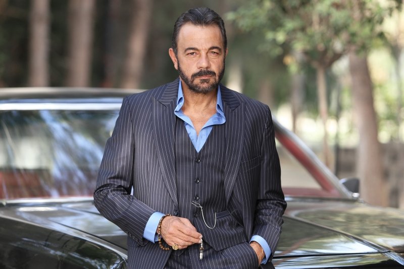 Kerem Alışık in a stripped grey formal suit in front of his car.